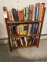 Full view of three shelves filled with assorted books on a wooden bookshelf.