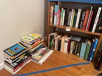 Books arranged on shelves and stacked on floor against wall showing multiple titles including film, sport, and biography topics.