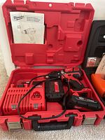 Milwaukee cordless drill in red plastic case with manual, charger, and battery visible