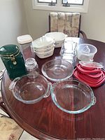 Photo of assorted Corning Ware casseroles, Pyrex glassware, canisters, and lids on wooden table.