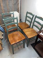 Four wooden dining chairs grouped together showing blue painted frames, brown wooden seats, visible wear and condition.