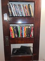 Sony BDP-S5500 Blu-ray player with remote control and multiple DVDs/Blu-ray cases arranged on dark wooden shelves.