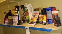 Shelf with various automotive fluids and cleaners including fuel stabilizer, brake fluid, WD-40, bug and tar remover, glass cleaner, acetone, tire cleaner, and car wash wax bottles.