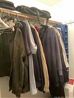 Hanging men’s shirts, blazers, jackets, and jerseys on hangers on a closet rod.
