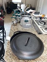 Photo showing Lodge cast iron covered pot in front with Wearever pots and pans behind including sauté pan with teal handles.