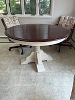 Full view of the round kitchenette table showing the wood top and the white pedestal base between two cushioned chairs.