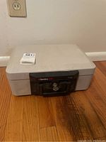 Closed view of light gray SentrySafe 1100 with black front panel and key lock, sitting on hardwood floor near an outlet.