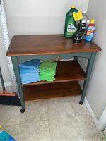 Front view of the wooden shelf with cleaning products and cloths on it showing its design and caster wheels.