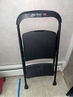 Front view of folded Easy Reach step stool showing black frame, two rubber steps, and handle with label.