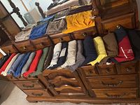 Folded assorted men's T-shirts arrayed on wooden dresser showing variety of colors and sizes large-XXL.
