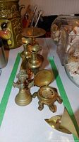 View of all brass items including turtle clock, vases, candle holder, bell, and sailboat figures arranged on white surface