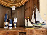 Photo showing 3 wooden decorative buoys painted blue and white with rope detail and 4 wooden sailboat models with fabric sails in various colors and small flags on the masts.
