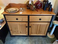 Front view of the cabinet showing two drawers over two cupboard doors with black framing and natural wood finish.