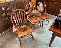 Three wood dining chairs, two with arms and one without, showing design and finish condition.