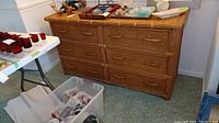 Front view of dresser showing six drawers and wicker style finish. Various items on top not included.