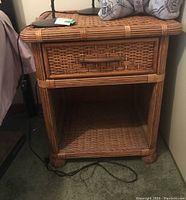 Front view of the wood end table showing one drawer with woven handle and open bottom shelf.