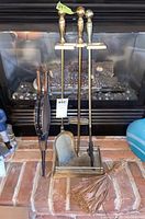 Fireplace tool set including stand with tools, bellow, and broom arranged in front of a fireplace.