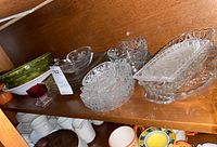 Shelf with glass serving dishes including clear cut glass bowls, rectangular dishes, and colored glass bowls plus ceramic plates below