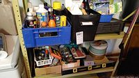 Wide shot of shelving with various boxes and containers of hardware and chemical products including spray cans and small parts.