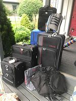 All bags arranged on porch; shows 5 wheeled luggage in black and blue, two cooler bags and duffle bags in front