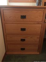 Front view of a light oak wood dresser showing four drawers with brass drop handles.