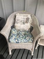 Painted white faux wicker chair with cushions, one blue and green floral patterned, the other beige with postal print.