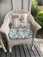 Front view of white faux wicker patio chair with blue floral seat cushion and beige patchwork back cushion.