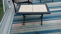 Side view of aluminum patio side table with tile top on outdoor striped rug, showing table legs and structure.