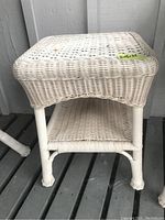 Full view of white faux wicker side table showing storage shelf and woven design.
