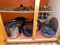 Cupboard with various pots, pans, baking pans, strainers and wire baskets showing contents of kitchen cookware lot.