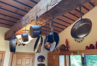 Photo showing multiple pots and pans hanging on kitchen wooden beam including copper and nonstick cookware along with metal kitchen utensils