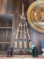 Wood and rope wall hanging mounted on wooden wall with decorative knots and four black wooden dowels, loop at top for hanging.