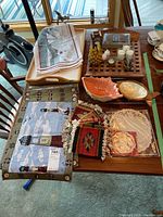 Wood and plastic lap tray, wooden serving tray with folded textiles including placemats and coasters, ceramic serving dishes, candles and holder on wooden grid, lace doilies