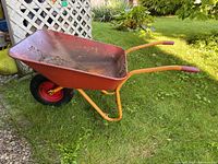 Side angle showing orange metal frame and red tub with rust inside placed on grass.