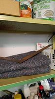 Shelf with folded thick gray speckled blanket and wooden wedge on top and some packaging behind