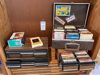 Wider shot of cassette tape holders, cassette tapes stacked, and 8-track case with cartridges inside.