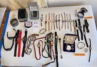 Wide view of the entire watch collection showing multiple wristwatches, electronic watches, watch parts, and pocket watches on a white cloth surface.