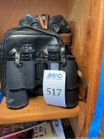 Front view of the Toko Seiki EDOGA binoculars with leather strap and partially visible leather case behind.