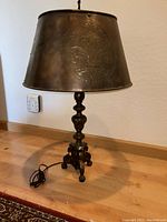 Full view of the antique bronze lamp showing the large metal shade with embossed Fleur de Lis and lamp cord on hardwood floor.