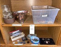 Multiple containers holding approx 95% pennies and 5% mixed coins, a glass Skippy jar, foreign coins, paper money, collectible coins and tokens, and a large plastic container of stamps labeled as such.