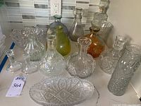 Collection of cut glass vases, decanters, and bowls in clear, green, and amber glass with ornate cuts and patterns on a kitchen counter