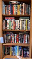 Full view of a wooden shelf filled with mixed DVDs and VHS tapes in cases, stacked tightly.