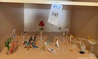 Full view of all glass art pieces on a wooden shelf showing assortment and variety