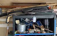 Overview of seven fishing rods in cloth cases on top of shelving with assorted gear below