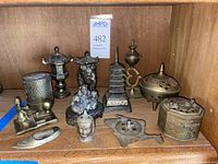 Photo shows a shelf with an assortment of brass and brass-look incense burners of varying shapes and motifs.