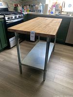 Full view of kitchen island in kitchen surroundings, showing wood top, stainless steel legs and lower shelf.