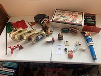 Overview of the lot on white folding table showing figurines, vehicles, magnets, lighter and light