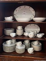 Full display of the china set arranged on wooden shelves showing various plates, cups, and serving pieces.