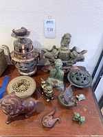 Overview of full lot showing stone incense burner, brass container, latticework burner, round lid, Buddha statue, brass foo dog, boat censer, frog, terracotta lion body, flame piece.
