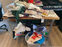 Five piles of folded graphic T-shirts on two-tier table, top view shows assorted colors and graphics
